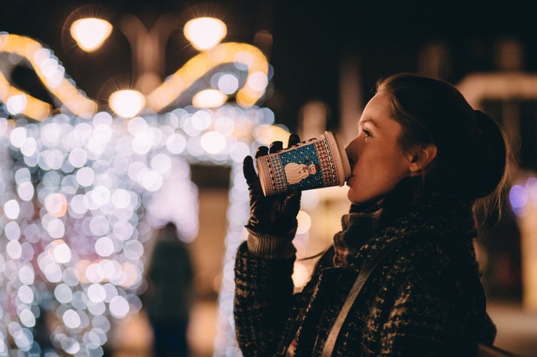 Christmas scene of woman in festively lit street, drinking from snowman cup