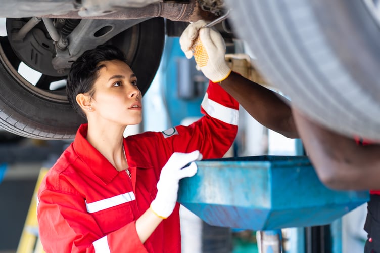 Black Male And Female trainee Mechanics Working Underneath Car Together Car maintenance and auto service garage. 