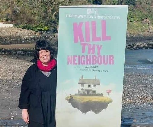 Artistic Director Chelsey Gillard with Kill Thy Neighbour play advertisement on Pembrokeshire beach.
