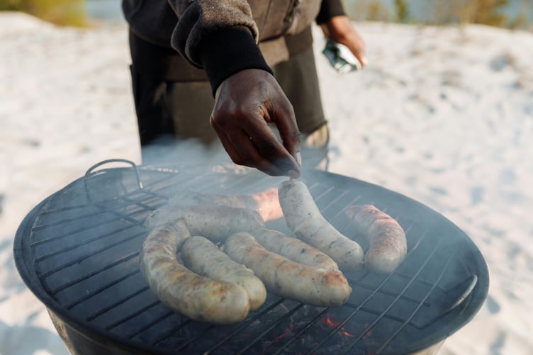 Man placing sausages on barbecue on beach