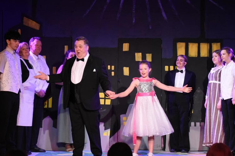 Drew as Oliver Warbucks and Hallie as Annie with other cast members