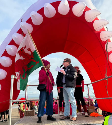 Côr y Môr were over the moon to receive a £500 share of funds raised at this year's Saundersfoot New Year's Day Swim. On the day choir members presented medals to the brave swimmers, of which there were 3,300! In the picture, Delwen Williams, on stage with DJ Benny Bond, waves the starter flag.